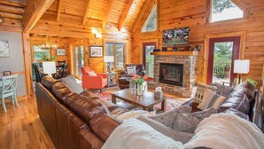 A log cabin interior with a fireplace, leather sofas, and a dining area. - Luxurious Log Cabin with Stunning Views (Sugar Mountain)