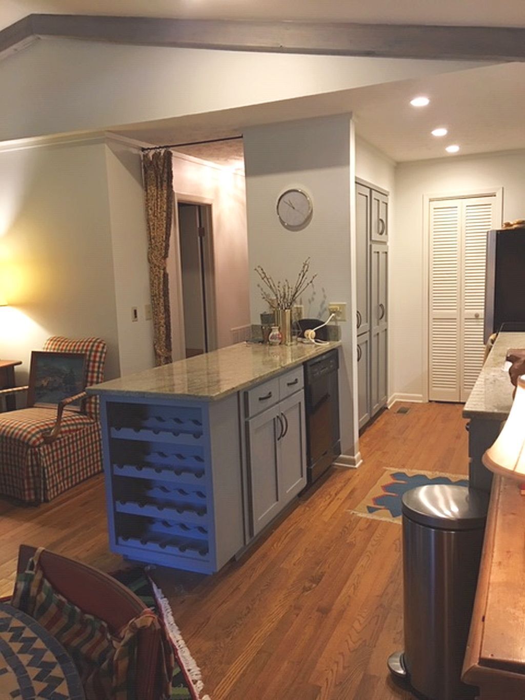 A compact kitchen with a central island, a dining area with a chair, and a trash can.