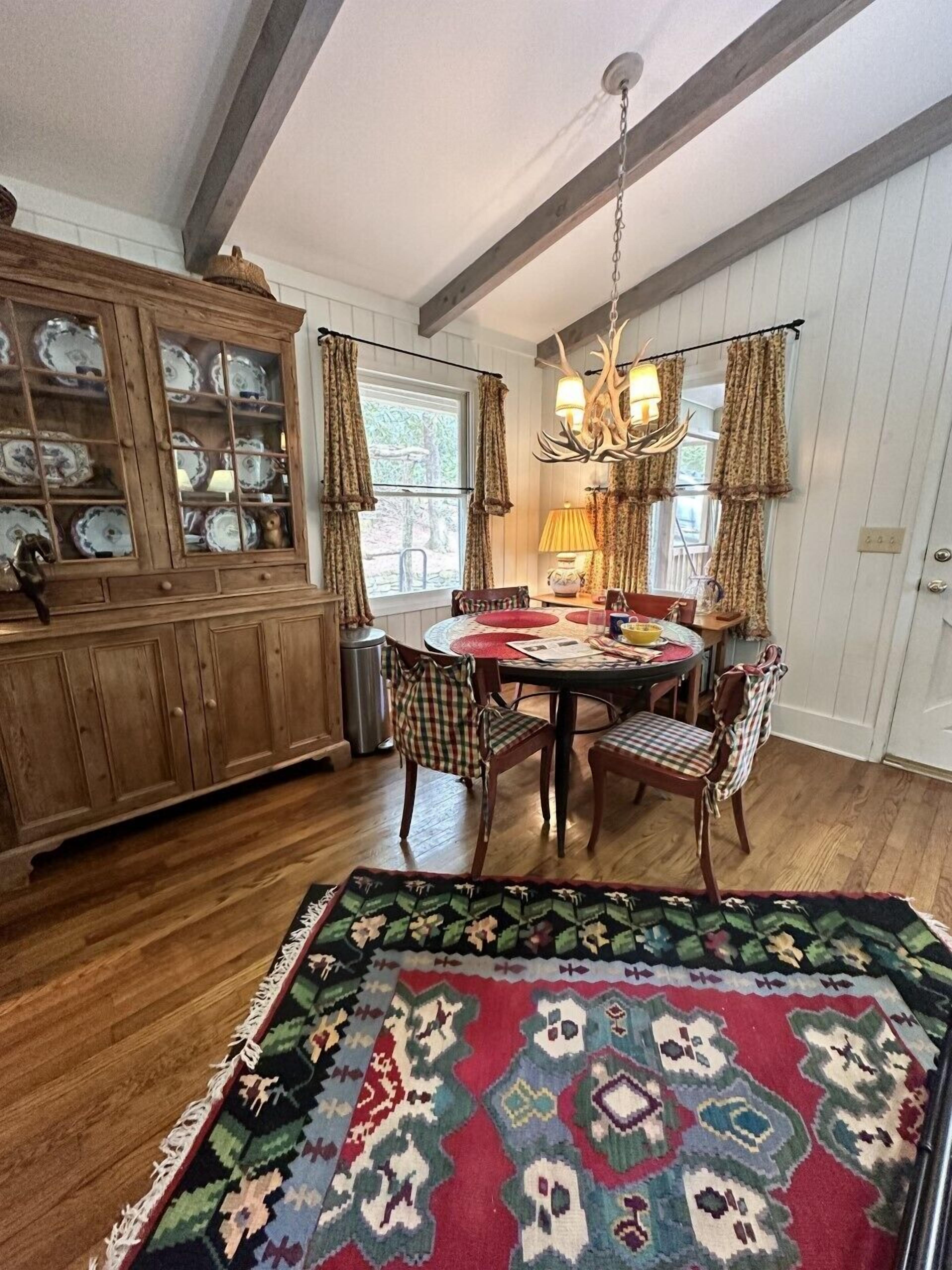A dining area with a wooden cabinet, a chandelier, and a patterned rug.