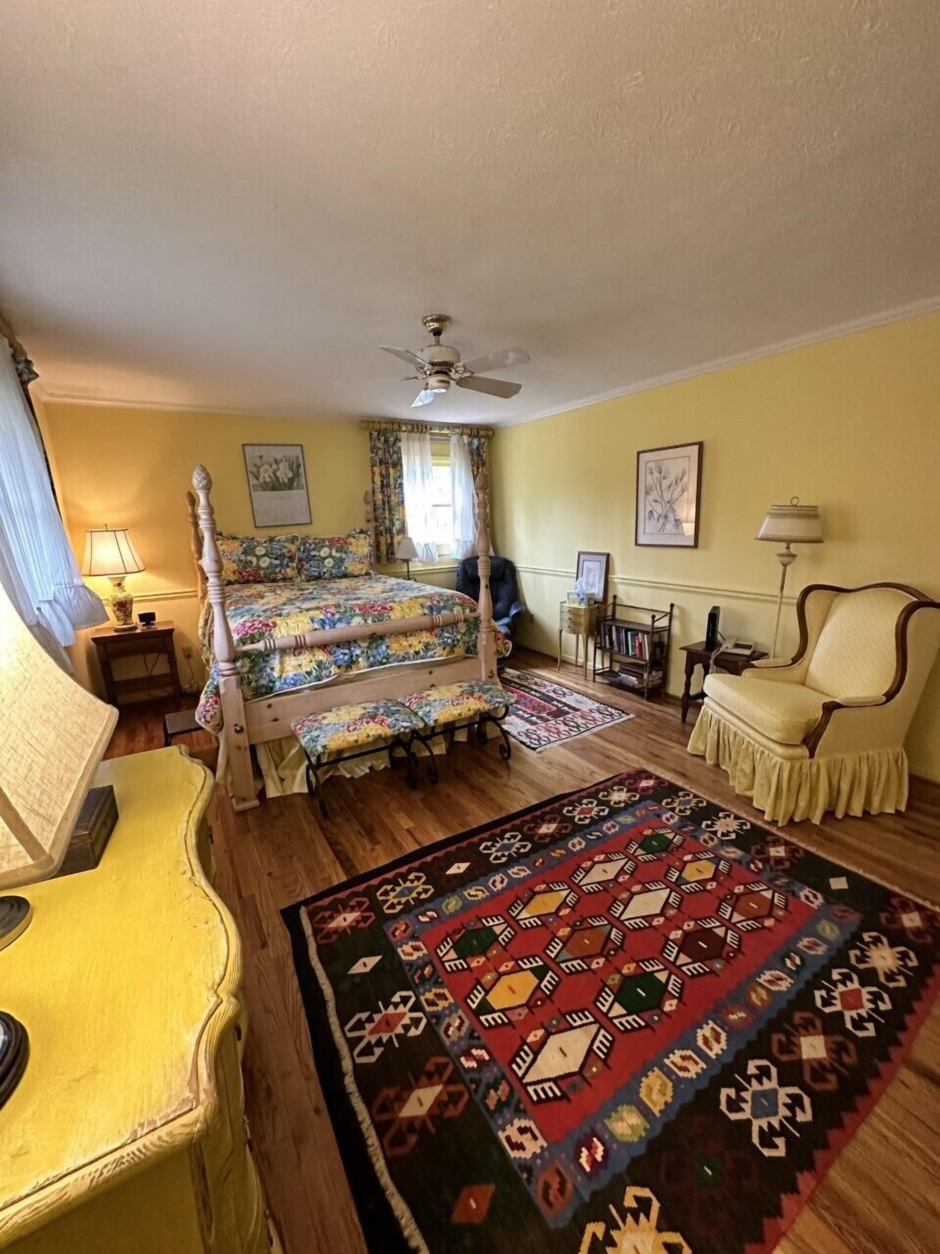 Een kamer met een bed, een stoel, een bureau en een vloerkleed.
