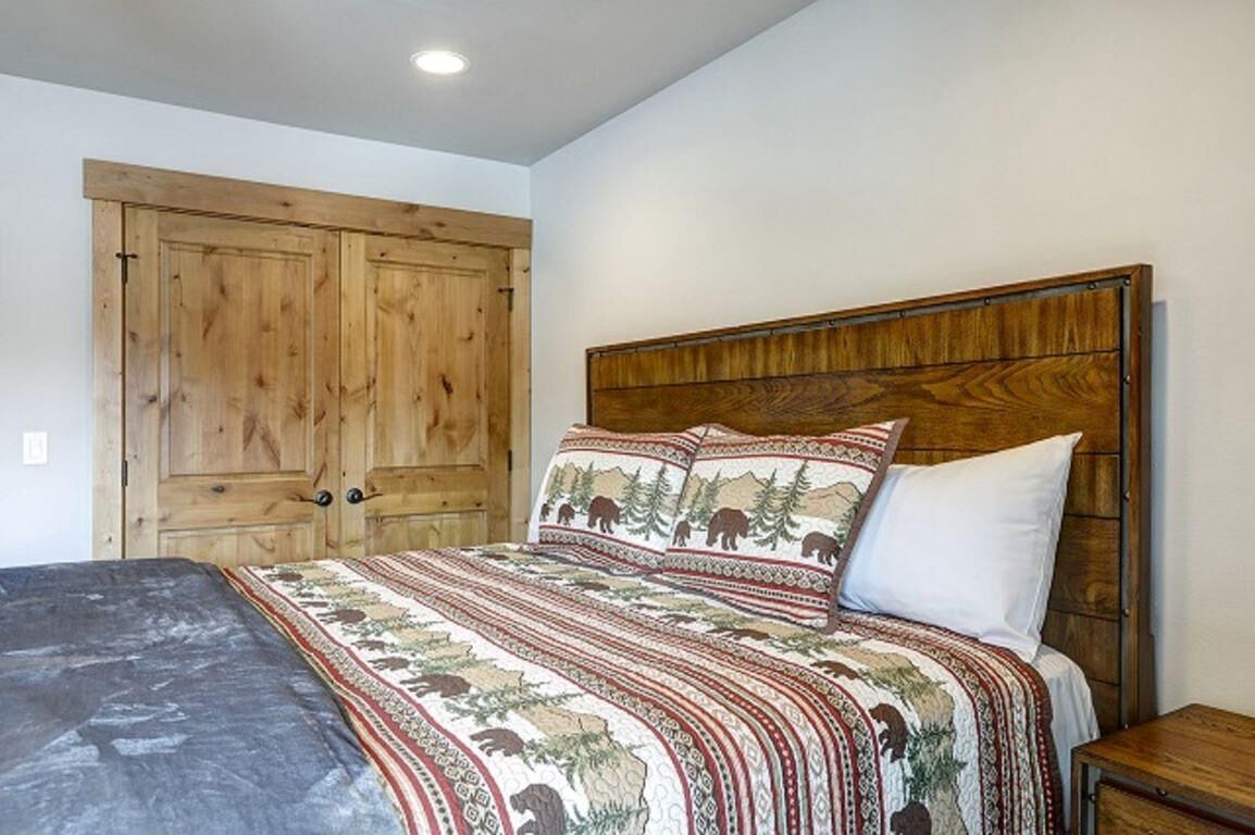 A bedroom with a wooden headboard, a bed with patterned bedding, and a wooden wardrobe.