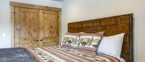 A bedroom with a wooden headboard, a bed with patterned bedding, and a wooden wardrobe.