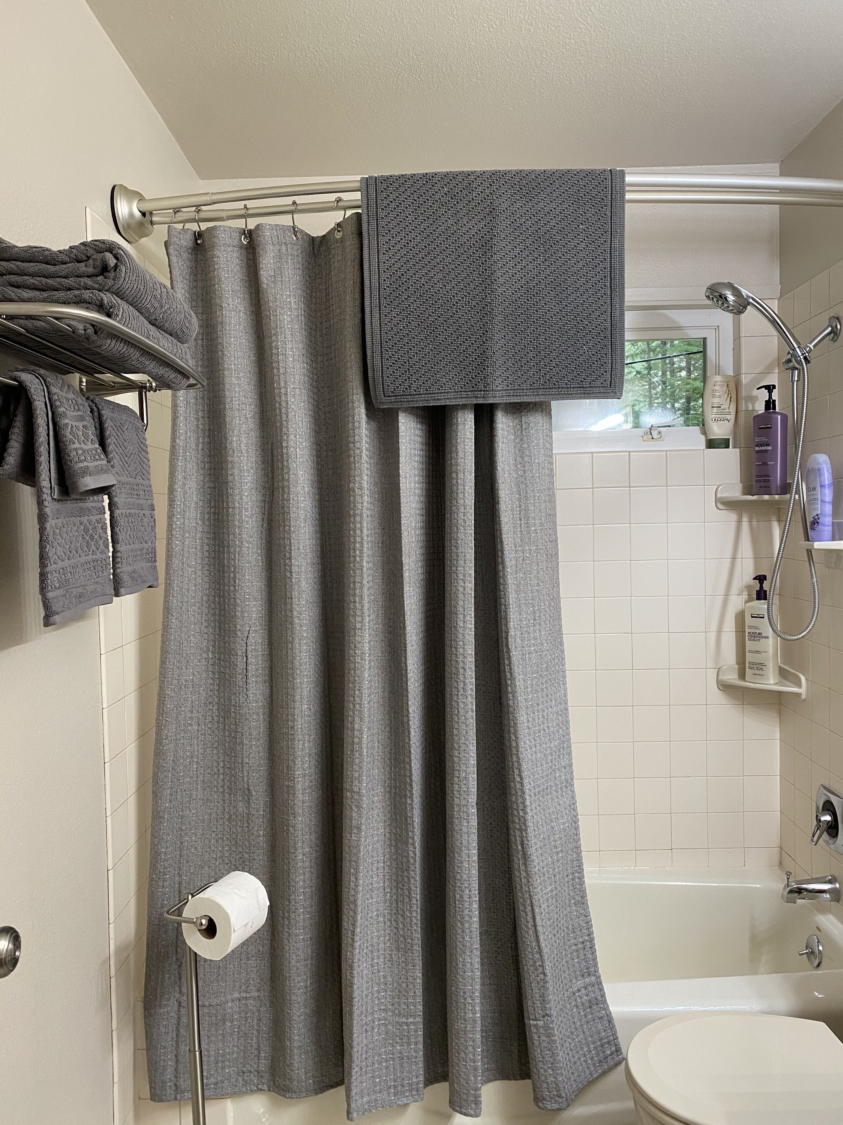 A bathroom with a shower curtain, a toilet, a sink, and a towel rack with folded towels.