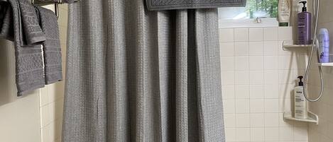 A bathroom with a shower curtain, a toilet, a sink, and a towel rack with folded towels.
