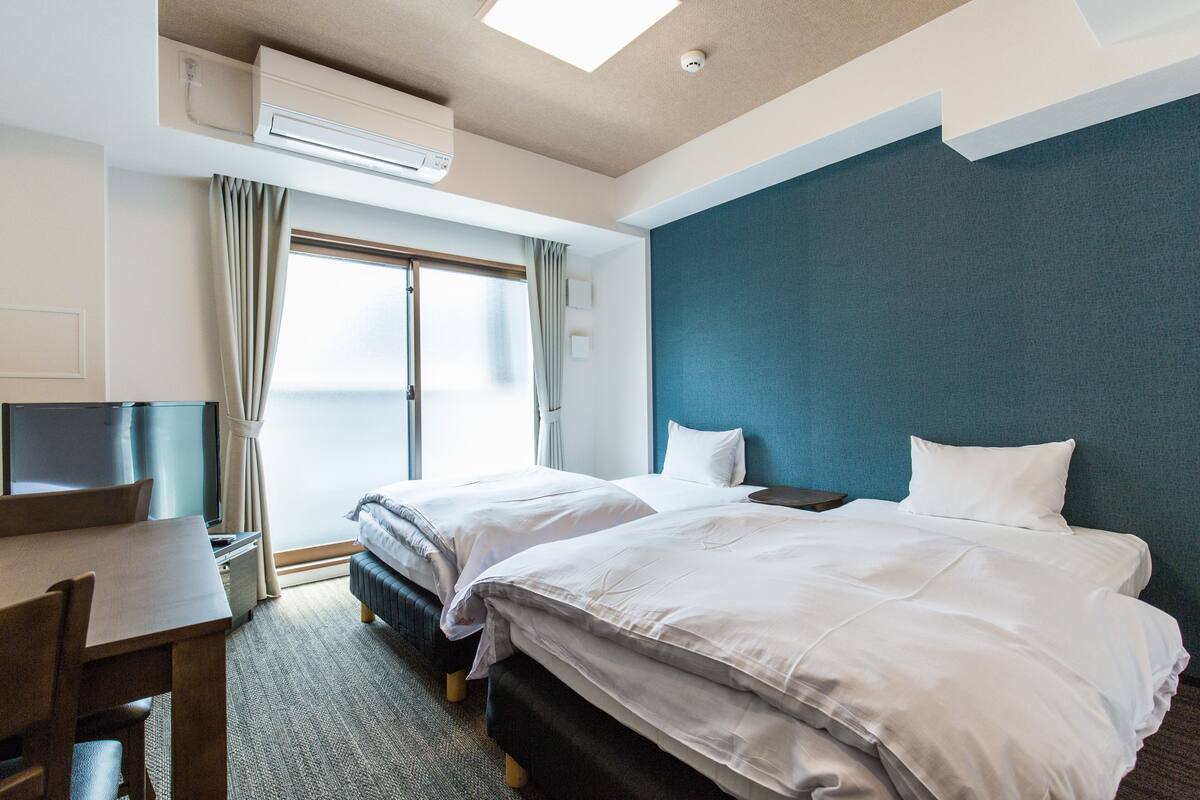 Ein Hotelzimmer mit zwei Betten, einem Schreibtisch, einem Fernseher und einer Klimaanlage.