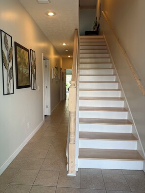 A hallway with a staircase, tiled floor, and wall-mounted artwork.