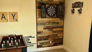 Et værelse med et bordtennisbord, dartskive, Scrabble-brikker og en trævægsdekoration.