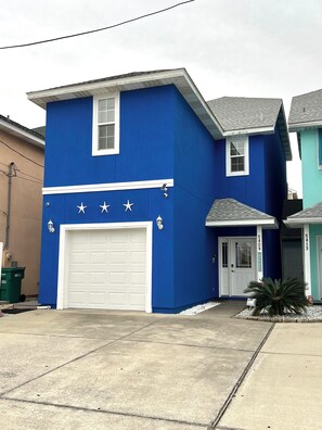 A two-story house with a blue exterior, a white garage door, and a small front porch.