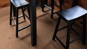 Una mesa de madera con un tablero de ajedrez en una habitación con ventanas amplias y vistas a árboles.