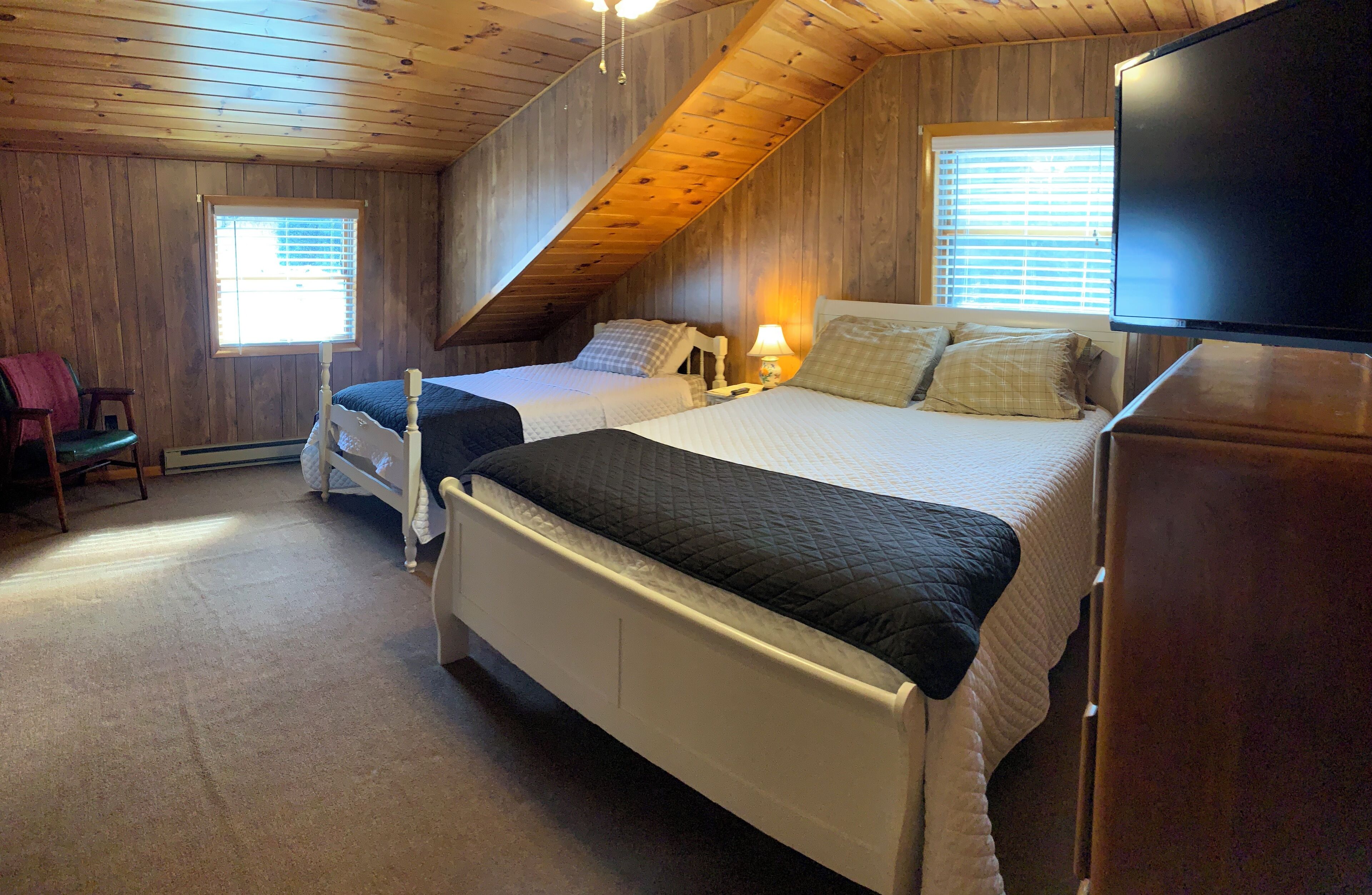 A bedroom with two beds, a television, and a chair.