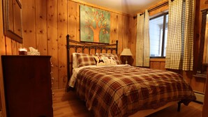 Ein Schlafzimmer mit Holzwänden, einem Bett, einem Nachttisch, einer Kommode und einem Fenster mit Karottenvorhängen.