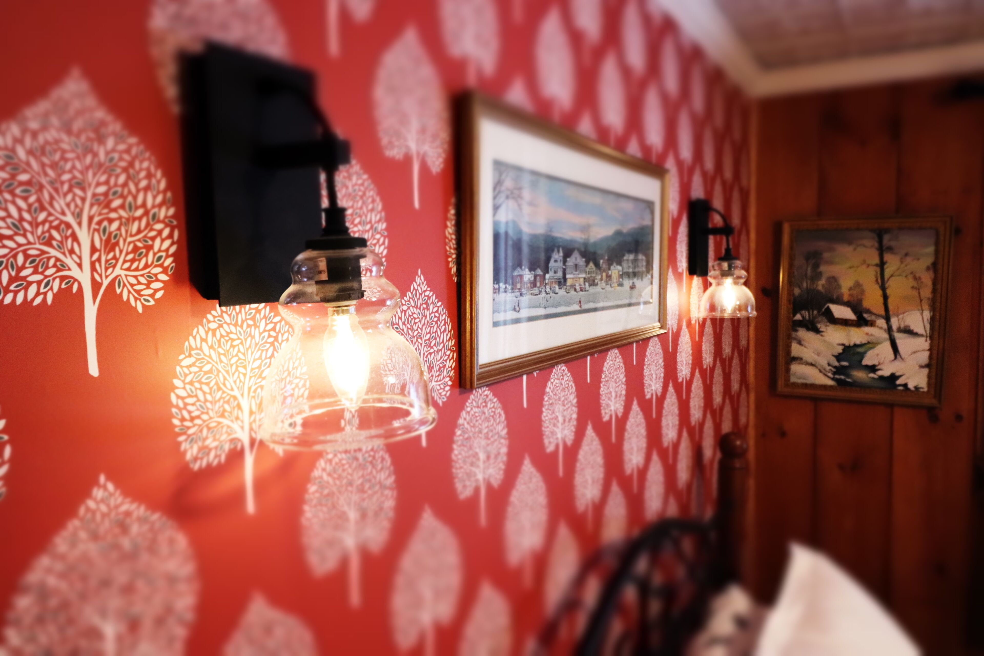 A room with a red patterned wall, a framed picture, and wall-mounted lights.