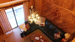 Ein gemütliches Blockhauss-Interieur mit Holzvertäfelung, einem schwarzen Ledersofa, einem Holztisch und einem Kronleuchter.