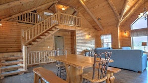 A log cabin interior with a wooden dining table, benches, and a staircase leading to an upper level. - Family Size Cabin with Kitchen, Fireplace, Hot Tub (Millersburg)