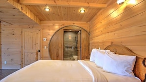 A wooden cabin bedroom with a bed, a circular window, and a shower area. - Family Size Cabin with Kitchen, Fireplace, Hot Tub (Millersburg)