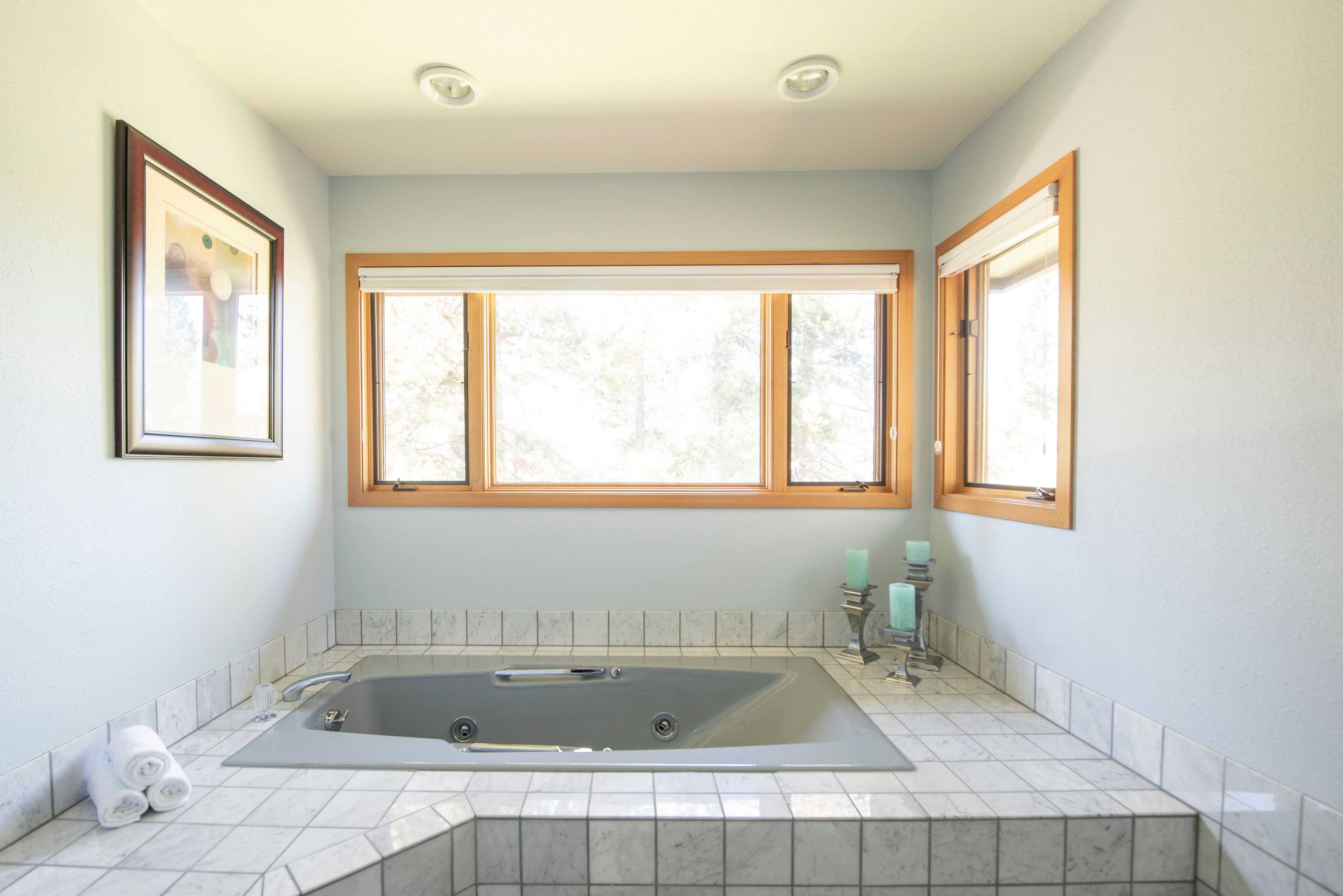 A bathroom with a large bathtub, a window, and a framed picture on the wall.