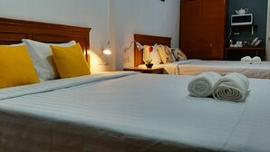 A hotel room with two beds, each with white linens and yellow pillows. There are rolled towels on the beds and a small table with a lamp between the beds. - Sala Bua Room Karon (Karon)