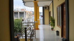 A corridor with yellow pillars, a metal railing, and a potted plant. - Fifawind Hotel Komodo (Labuan Bajo)