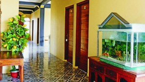 A hallway with a tiled floor, wooden doors, a potted plant, and a fish tank. - Fifawind Hotel Komodo (Labuan Bajo)