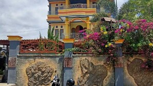 A multi-story house with a balcony, a scooter parked in front, and a decorative wall with plants. - Fifawind Hotel Komodo (Labuan Bajo)