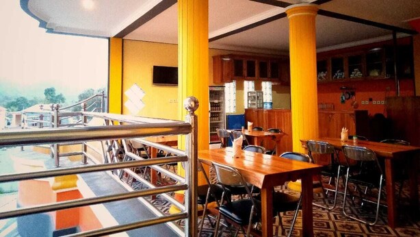 A restaurant with yellow pillars, a wooden dining area, and a view of the outdoors. - Fifawind Hotel Komodo (Labuan Bajo)