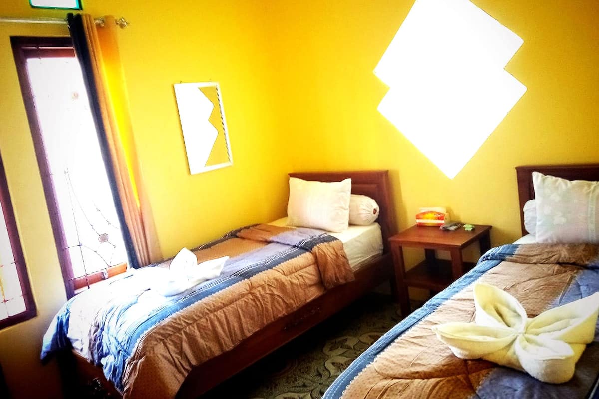 A room with two beds, a small table, and a wall-mounted picture frame.