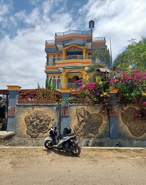 A multi-story house with a balcony, a scooter parked in front, and a decorative wall with plants.