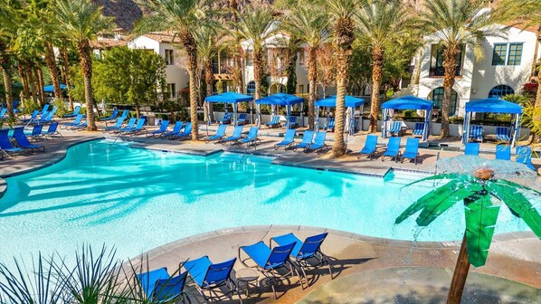 Relax by the resort pool surrounded by palm trees and a mountainous backdrop.