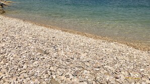 Una playa pedregosa con agua cristalina y una costa lejana.