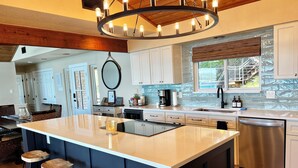 Una cocina moderna con una isla grande, taburetes de bar, horno empotrado y lavavajillas de acero inoxidable.