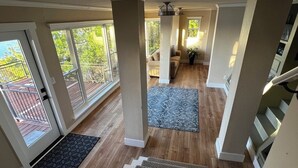 Un interior amplio con una escalera que lleva a un balcón, ventanas grandes y una zona central con alfombra y mobiliario.