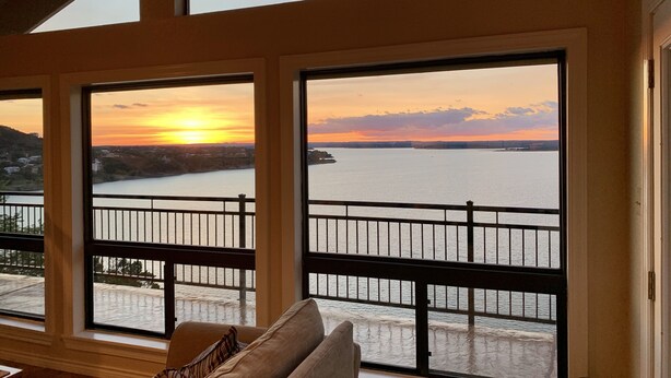 Una habitación con ventanas amplias que dan a un cuerpo de agua y al atardecer.