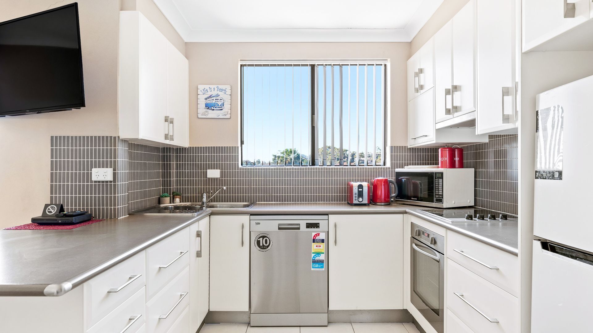 A modern kitchen with a dishwasher, microwave, and a window with blinds.