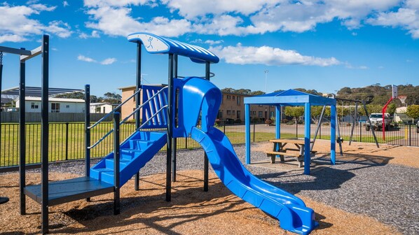 A playground with a blue slide, climbing area, and picnic table.