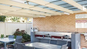 Un patio al aire libre con muro de ladrillo, un aparato a gas y una mesa con sillas.