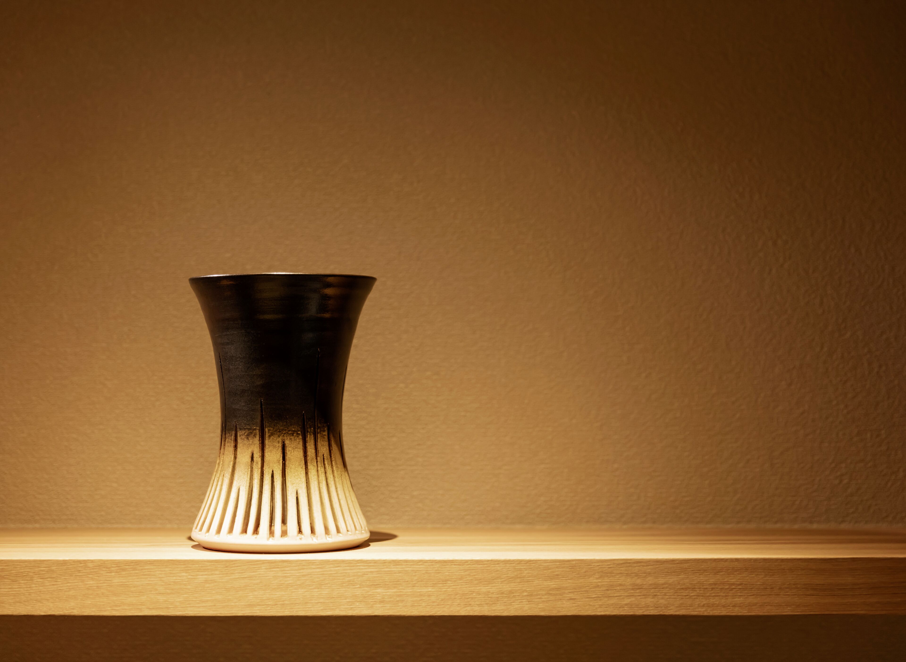A metallic vase with a tapered design on a wooden surface against a plain wall.