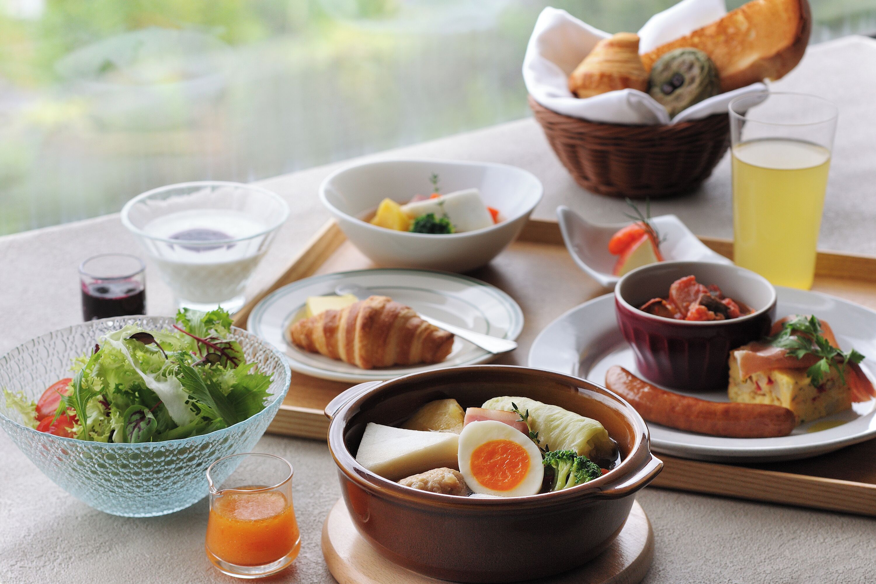 Ein Frühstücksbuffet mit verschiedenen Speisen, darunter ein Salat, Suppe, ein Croissant und ein Glas Saft.