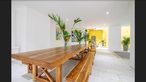 Een lange houten eettafel met banken, omringd door witte muren en potplanten.
