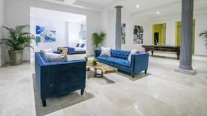 Een ruime lobby met twee blauwe banken, een houten salontafel en een piano.