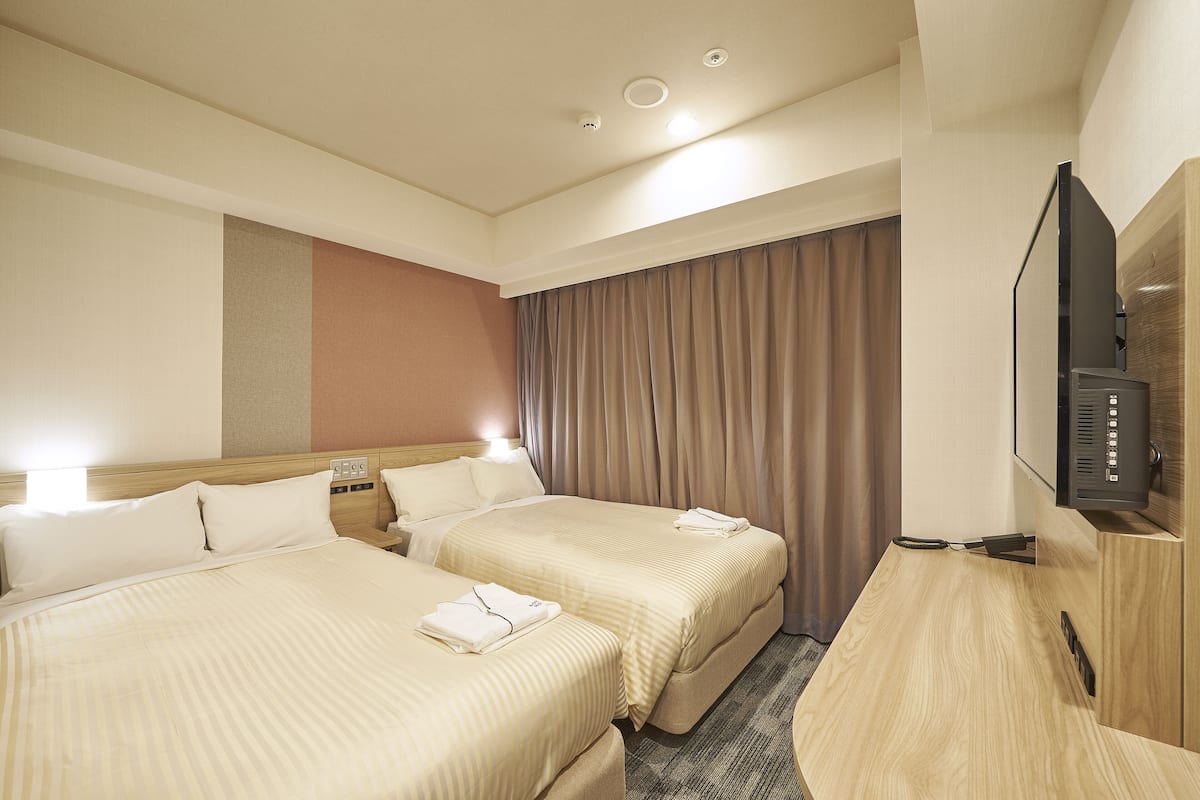 A hotel room with two beds, a TV, and a wooden desk.