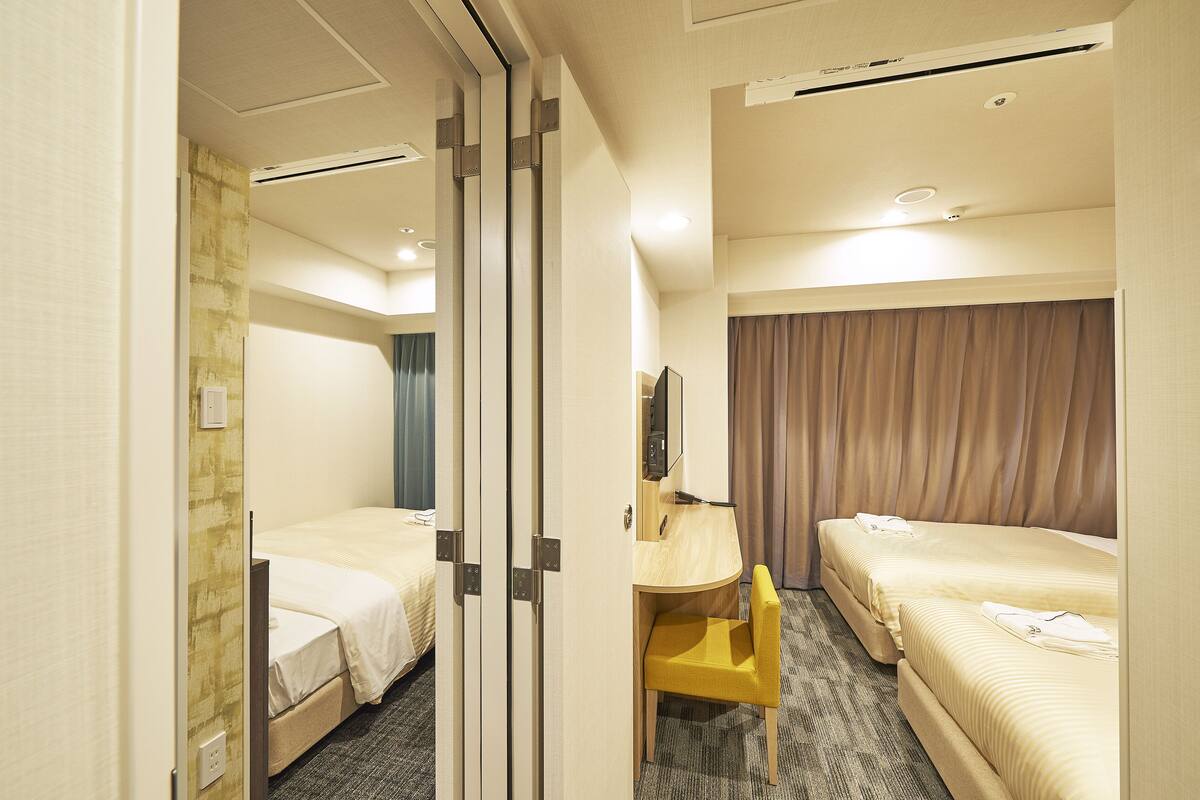 A hotel room with two beds, a desk, a chair, and a mirror.