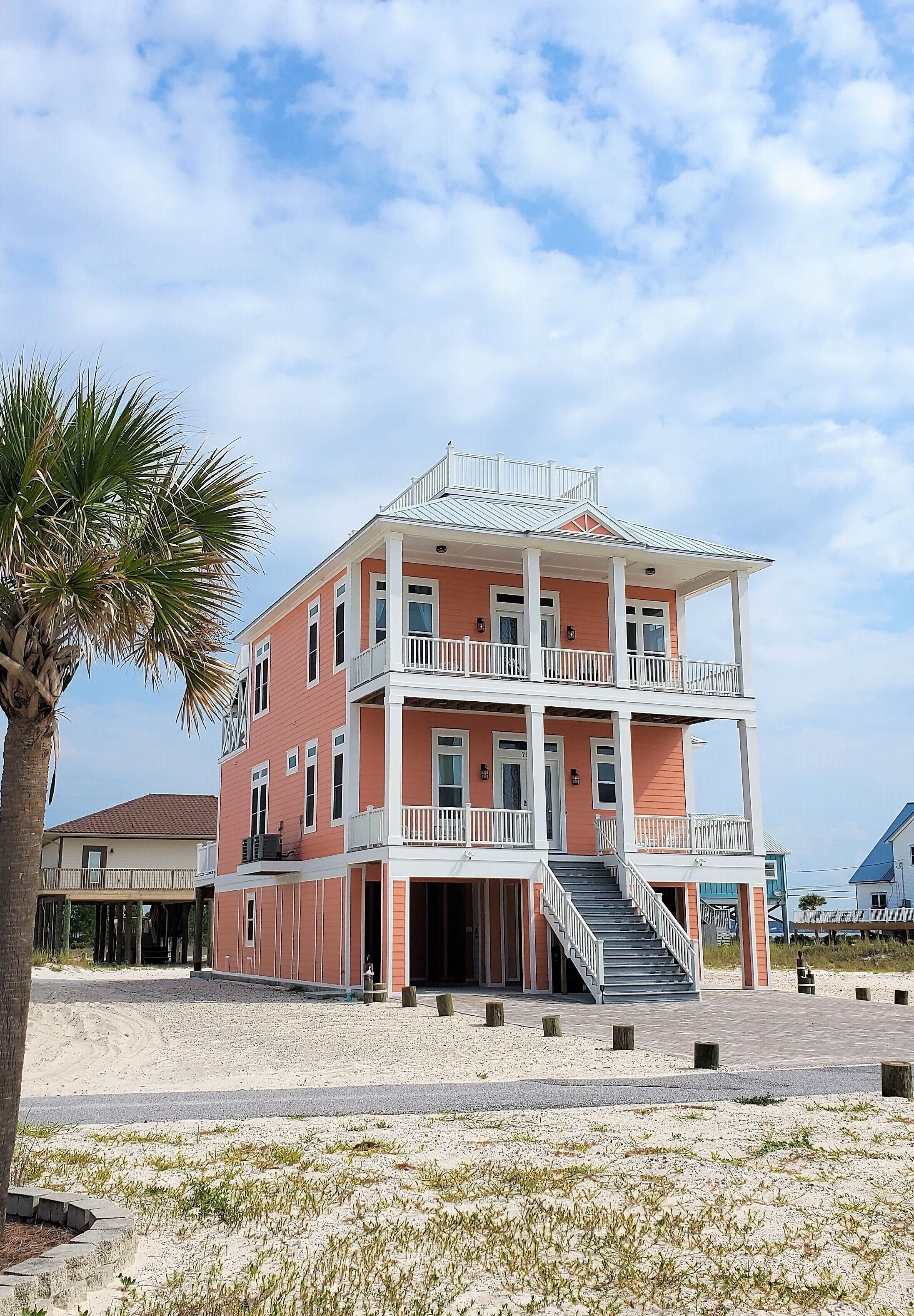 Un immeuble à plusieurs étages situé en bord de mer, doté de balcons et d’un escalier menant à l’entrée.