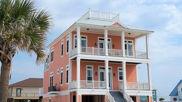Un immeuble à plusieurs étages situé en bord de mer, doté de balcons et d’un escalier menant à l’entrée.
