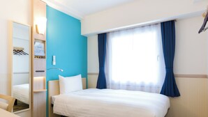 Una habitación de hotel con cama, escritorio, espejo, armario y ventana con cortinas.