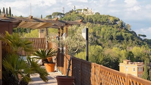 A terrace with a view of a hilltop building, wooden railing, and potted plants.