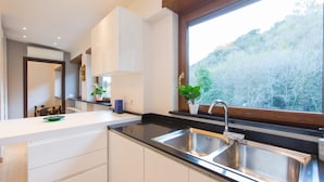 A modern kitchen with white cabinets, a black countertop, stainless steel sink, and a window with a view of a forest.