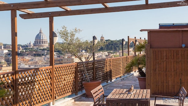 A wooden pergola with a bench and a table, overlooking a cityscape with historic buildings and a dome structure.