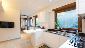 A modern kitchen with white cabinetry, a built-in oven, and a large window providing a view of greenery.