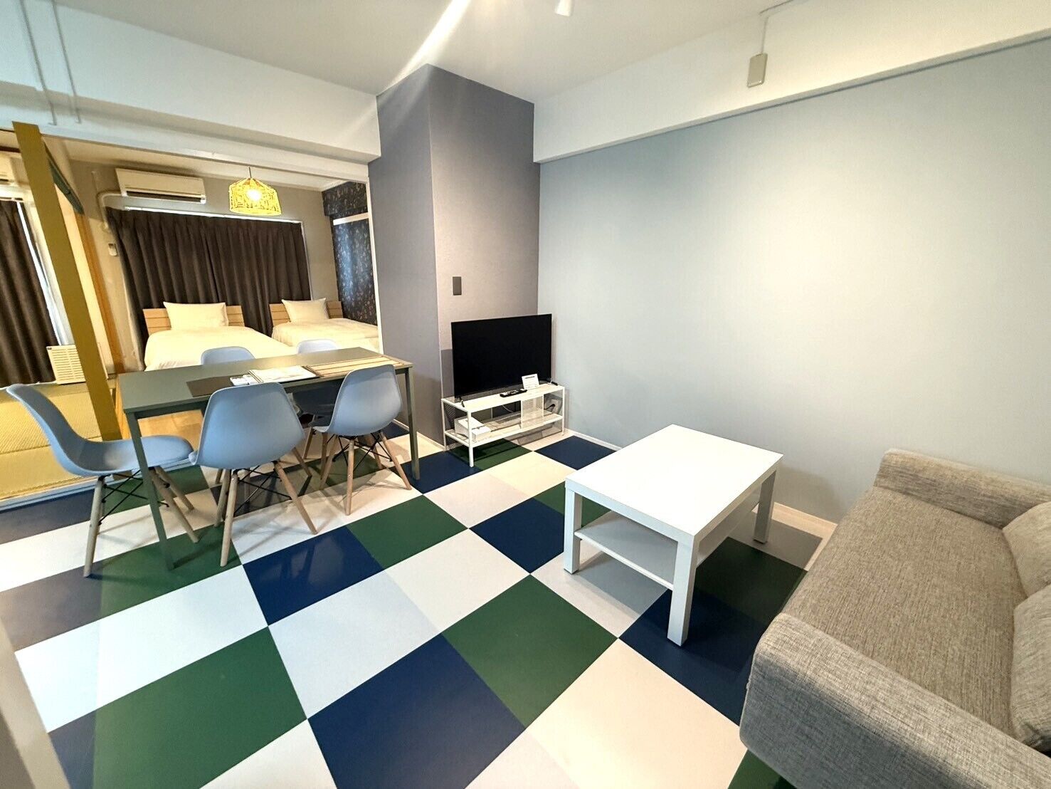 A modern hotel room with a bed, a dining area, a TV, and a checkered floor.