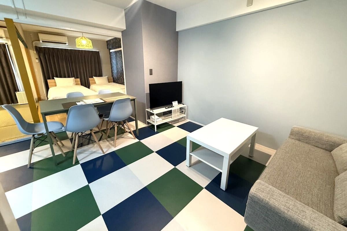A modern hotel room with a bed, a dining area, a TV, and a checkered floor.